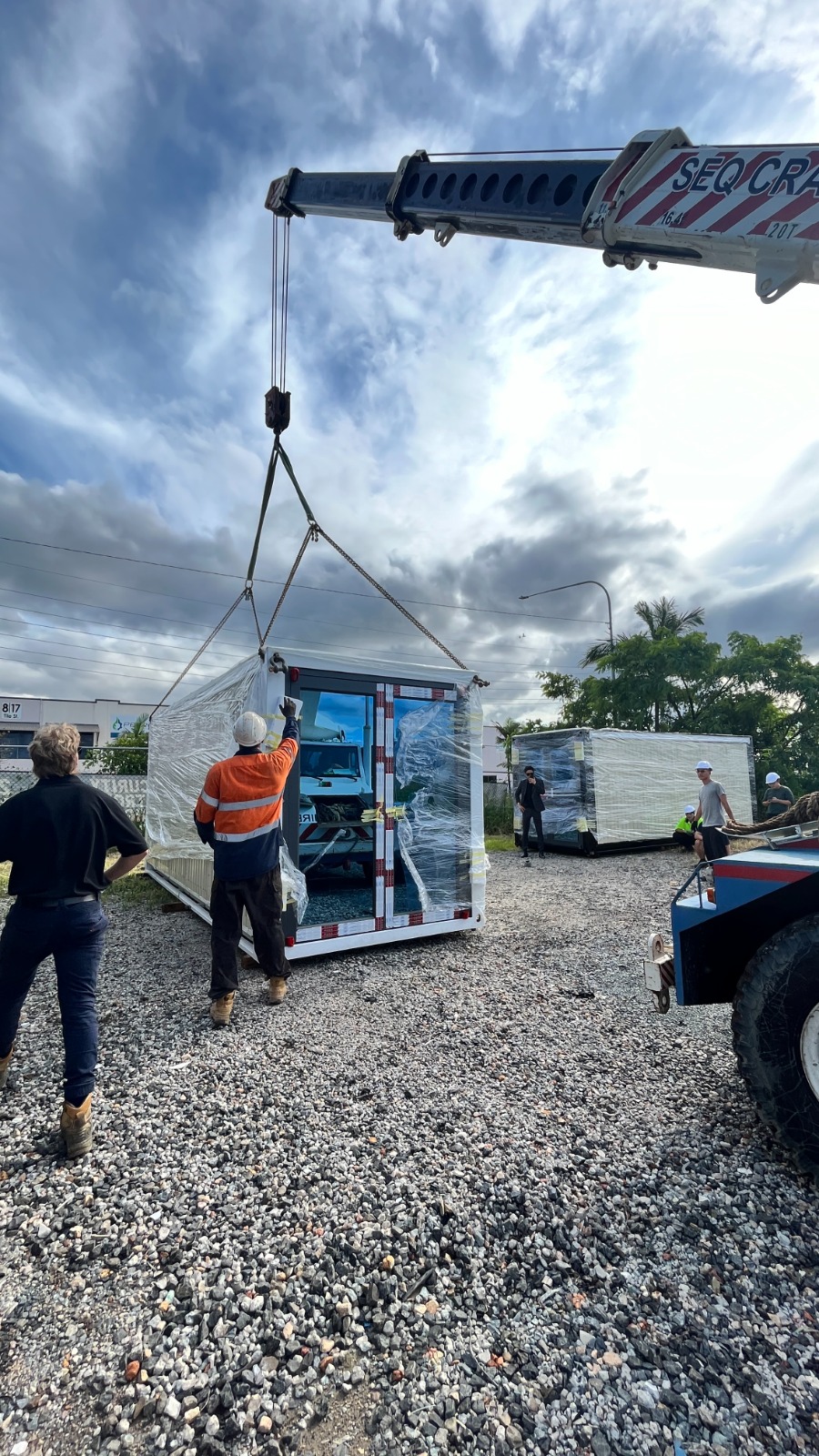 Crane operator lifting a shrink-wrapped Eco Nest House module off the delivery truck