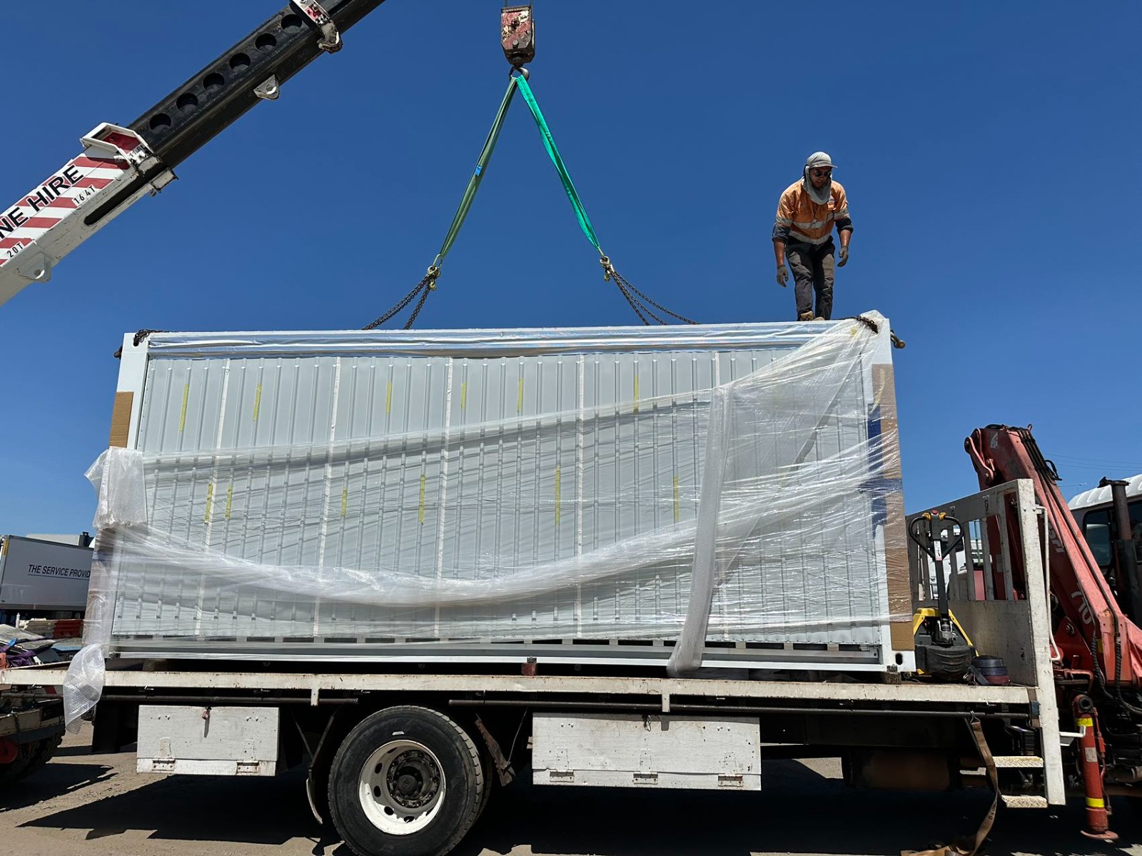 Worker guiding a suspended module into position on site, high above the ground